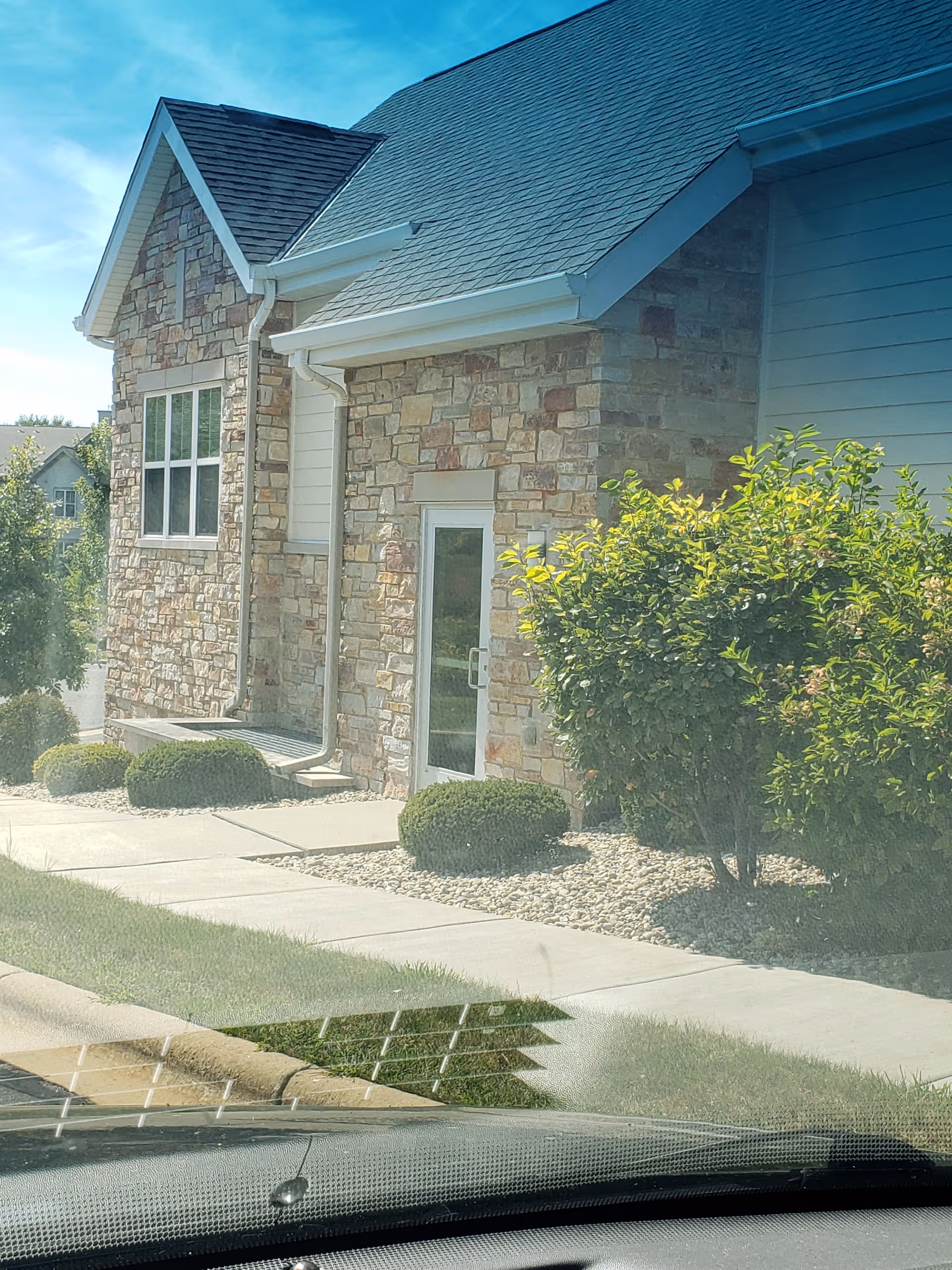 Stone facade building front entrance with landscaped shrubs and a clear blue sky.
