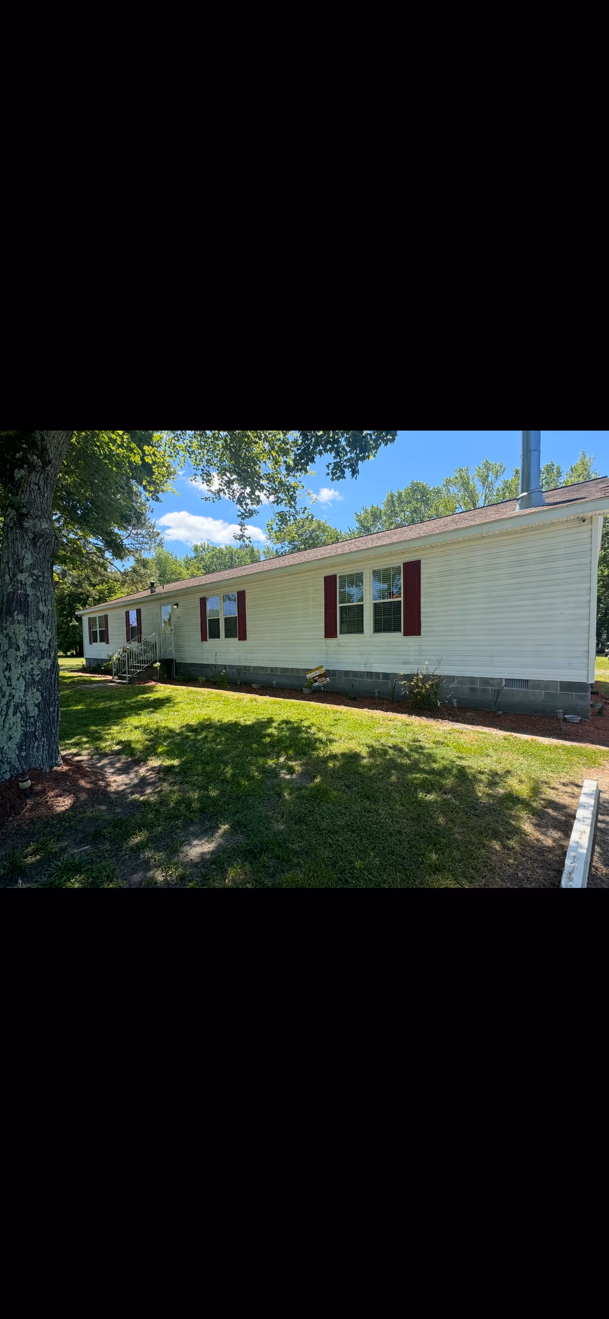 Exterior view of a single-story senior care building with white siding, red shutters, and lawn.