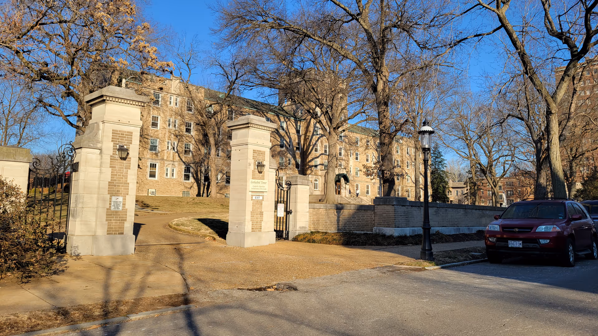Stone entrance gates frame a brick senior living building with a parked car nearby.