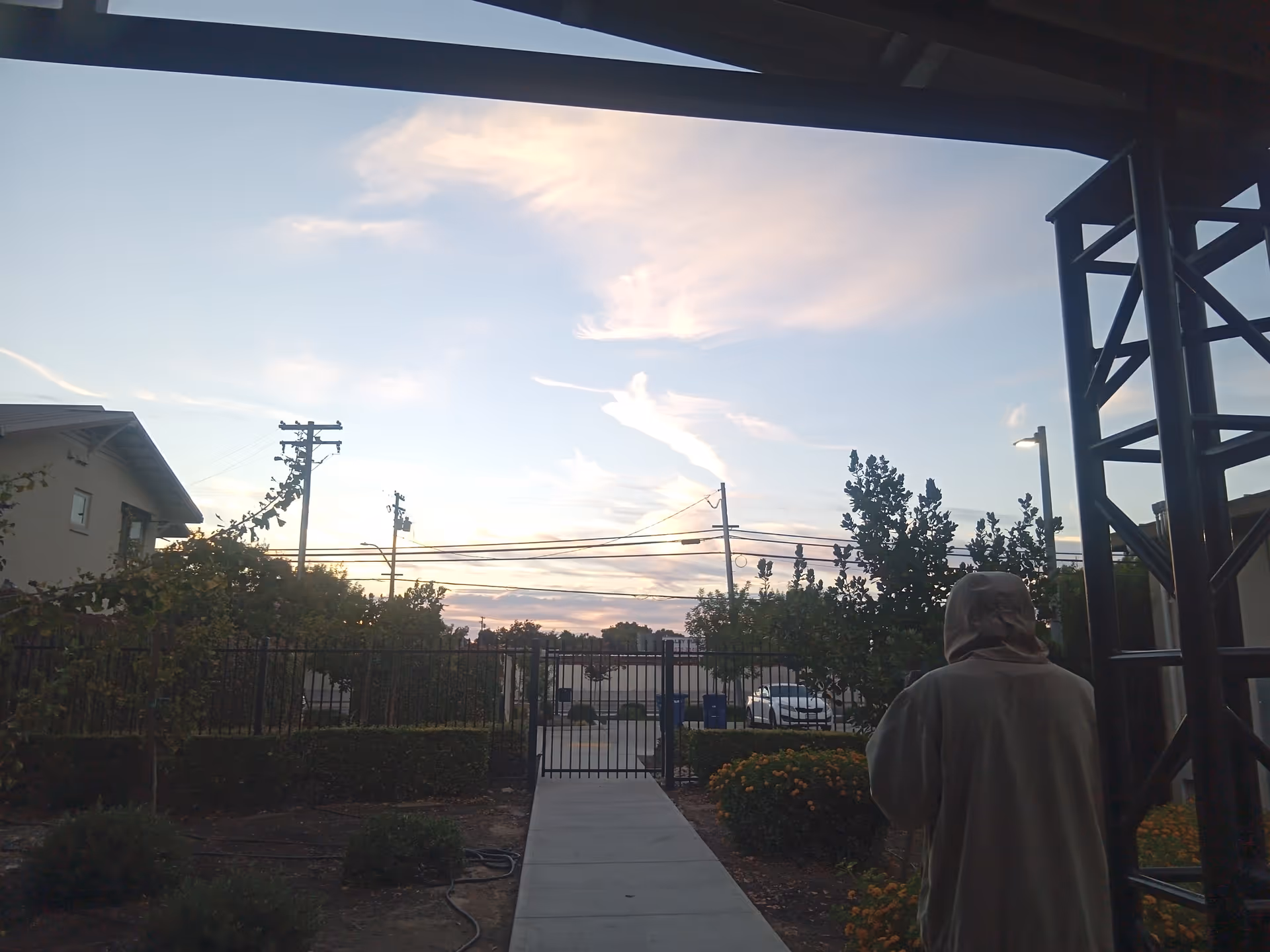 Sunset sky over a gated walkway at a senior living facility, with a person facing away.