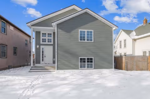 Front exterior of a gray two-story building in snow with neighboring houses.