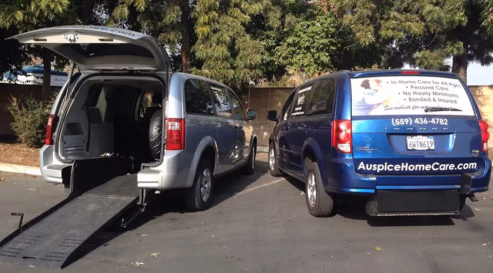 Two wheelchair-accessible vans parked in a lot outside, branded with Auspice Home Care & Transportation.