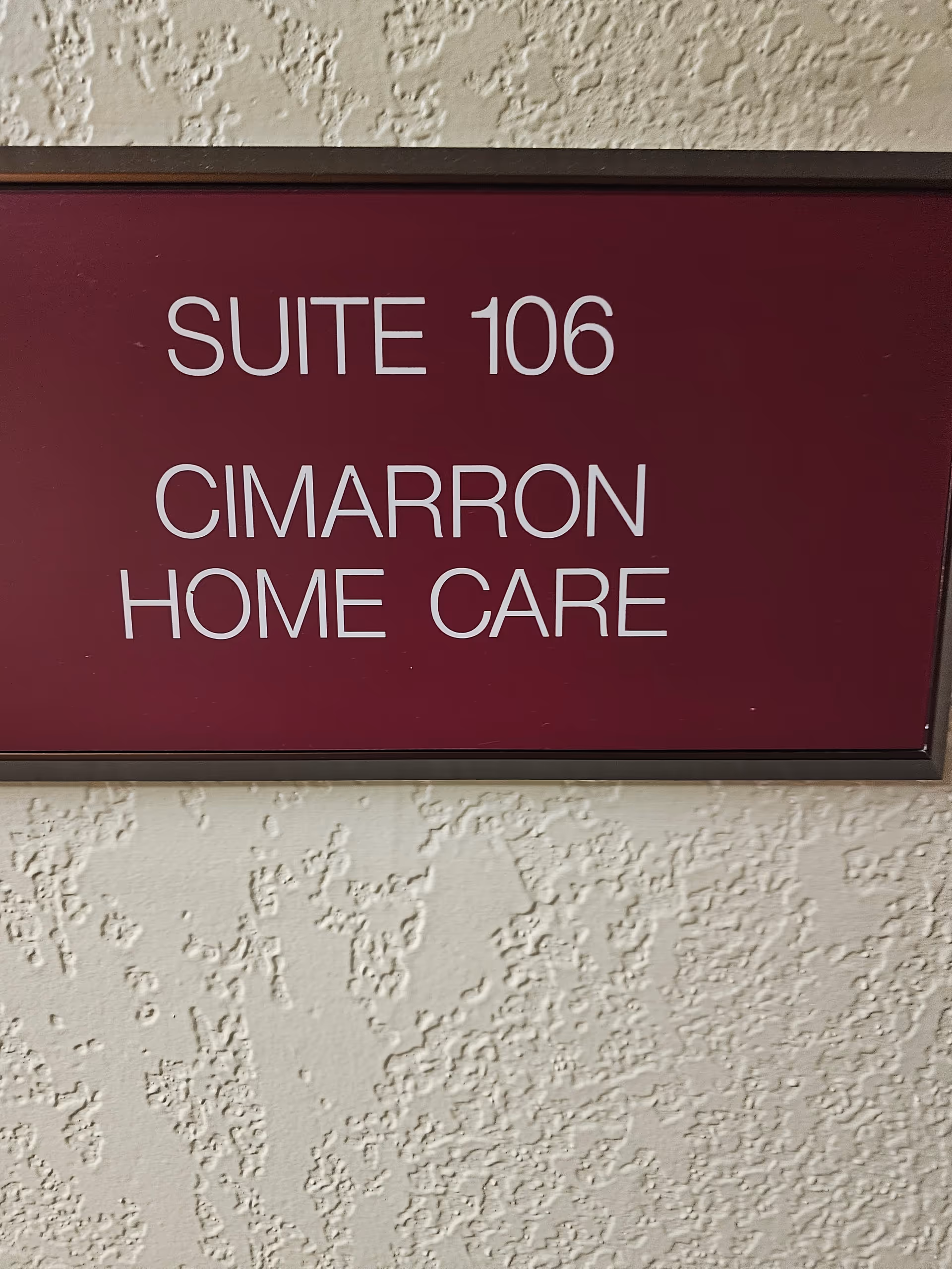Maroon sign reading Suite 106 Cimarron Home Care mounted on textured wall