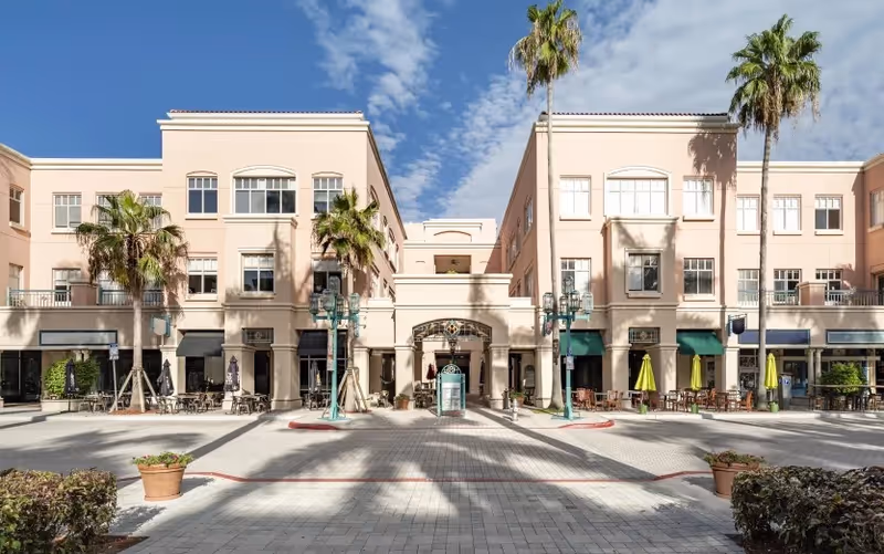 A peach-colored senior living campus with a central plaza, palm trees, and outdoor seating.