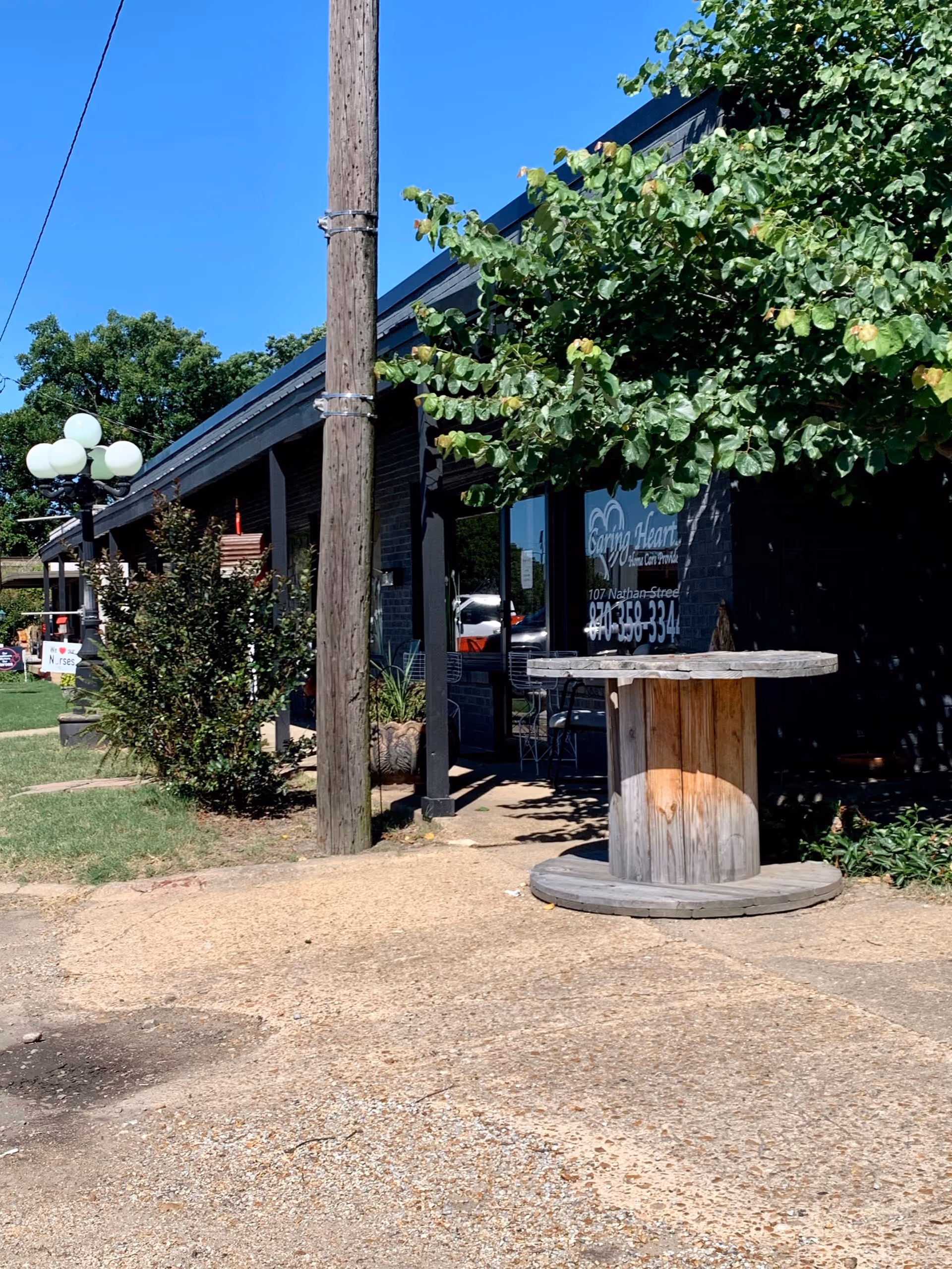 Exterior view of Caring Hearts Home Care with outdoor seating, trees, and a wooden spool table.
