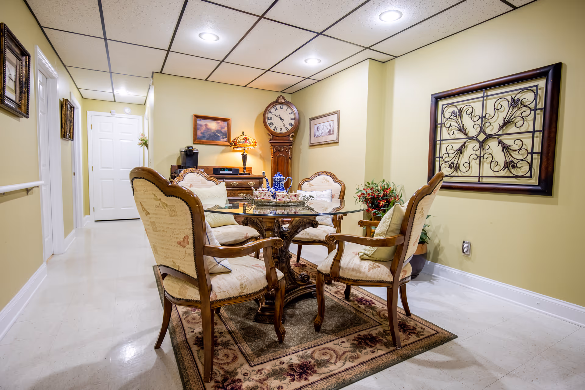 Elegant dining area with glass round table, upholstered chairs, rug, wall clock, and decor.