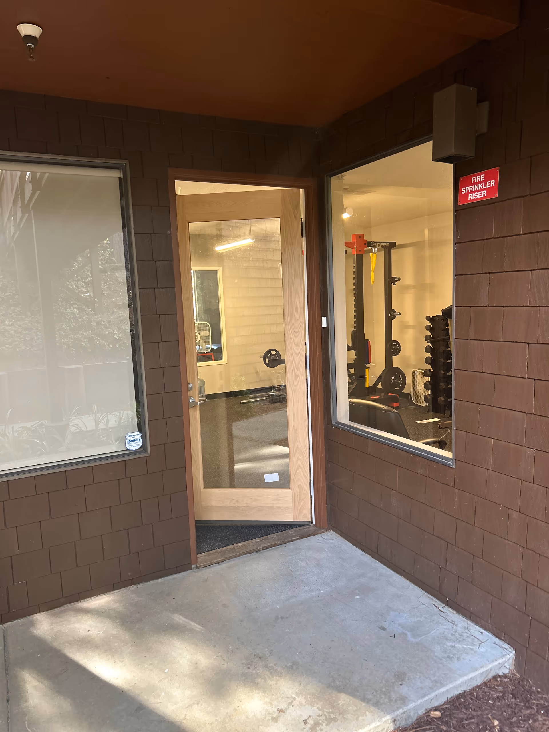 Exterior entry opens to an indoor gym with weight rack and equipment.