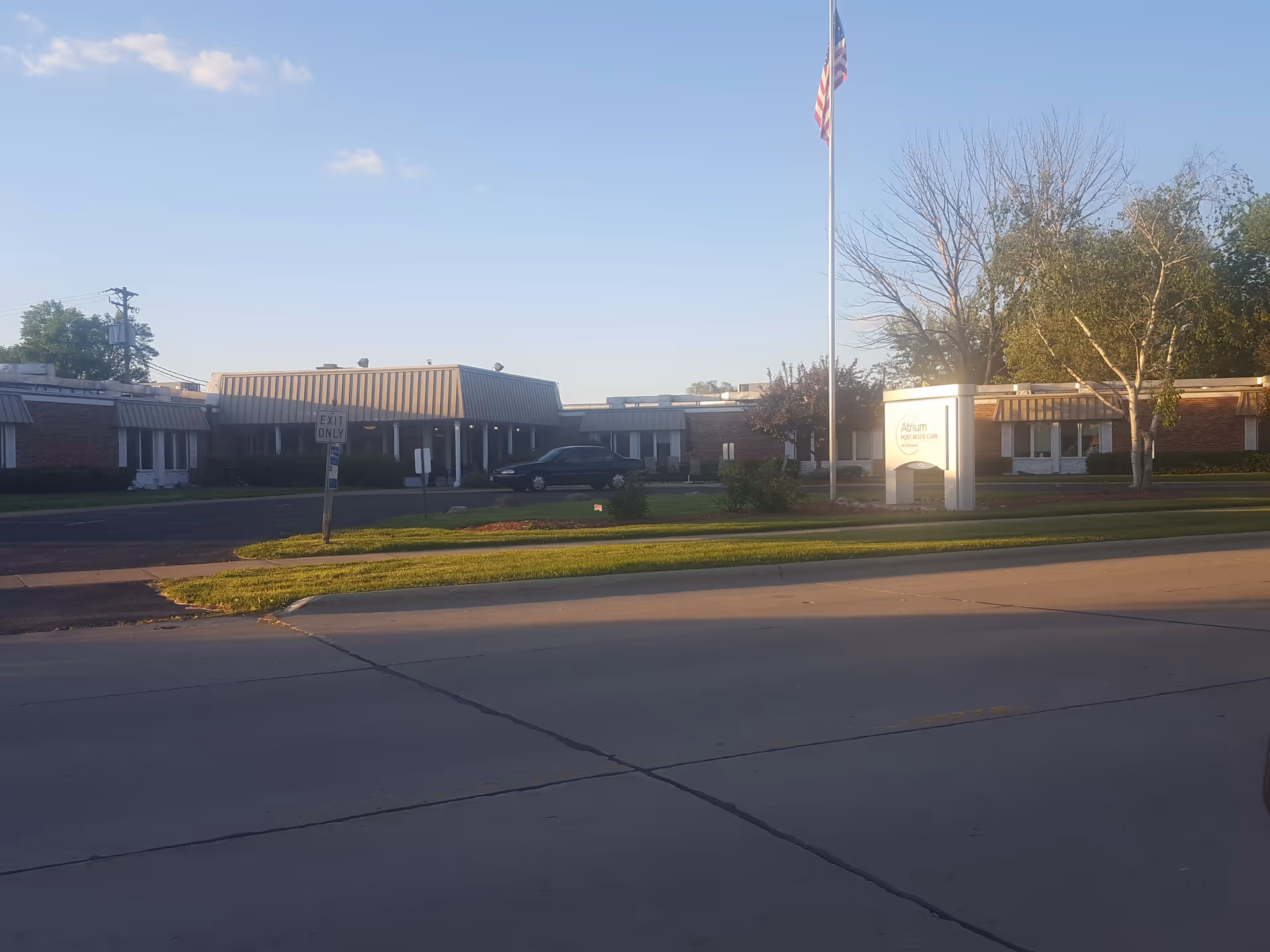 Exterior view of Meadowbrook at Oconto Falls, with flagpole and single-story brick building.