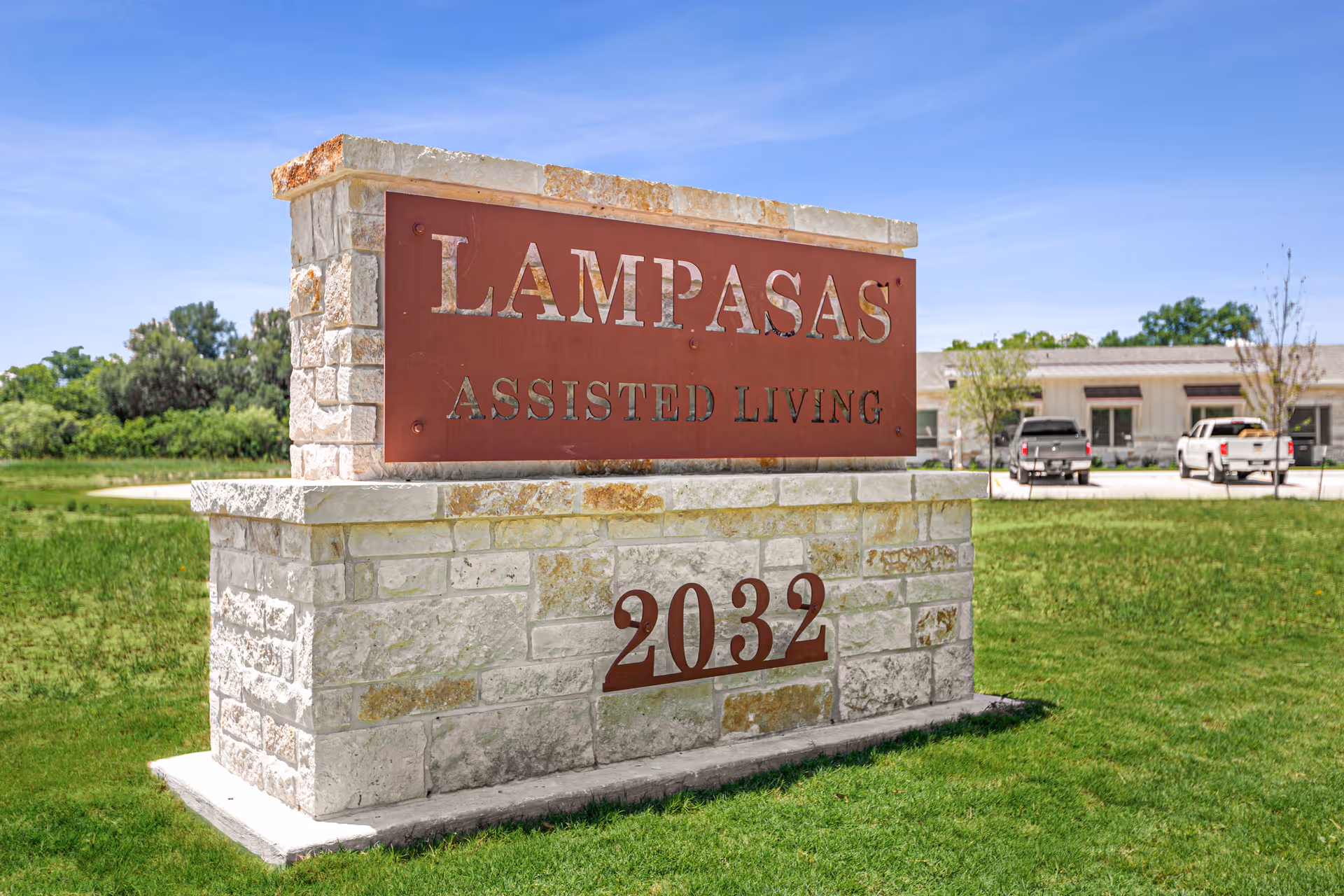 Stone sign reads Lampasas Assisted Living on a grassy lawn with a building in the background.