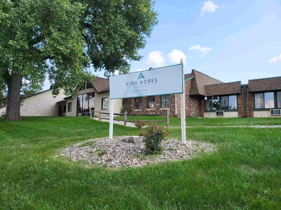 Front view of Pine Acres Rehabilitation & Care Center with a sign and green lawn.