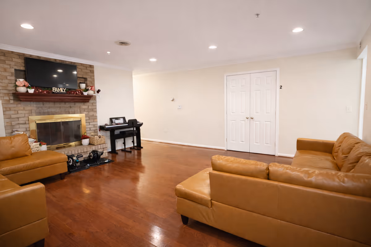 Spacious living room with leather sofas, a brick fireplace, TV, and white double doors.