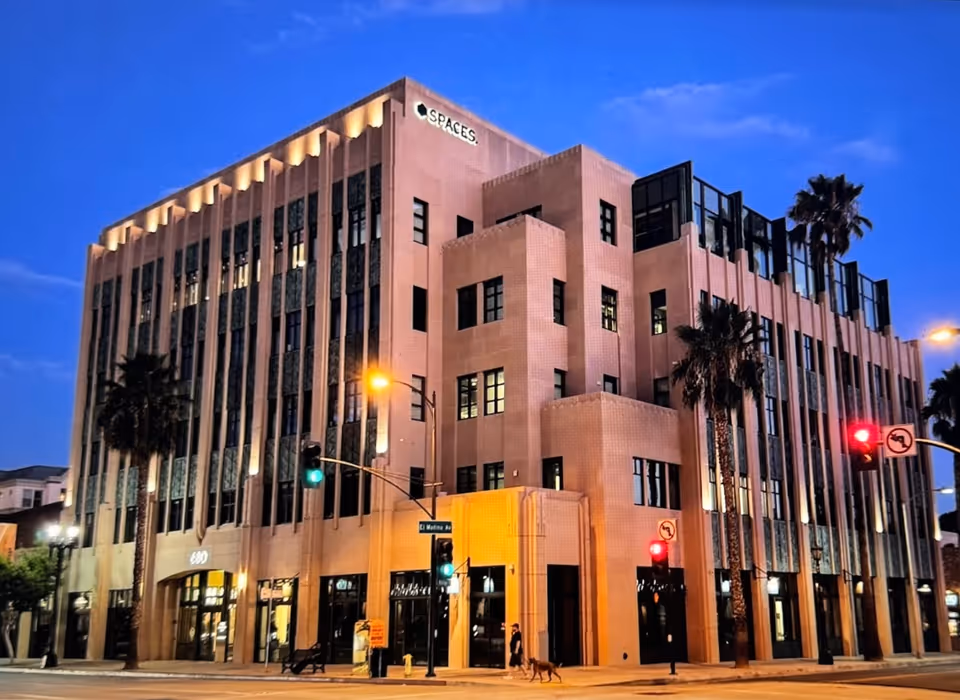 A modern multi-story building with tall windows at dusk, streetlights, and palm trees.