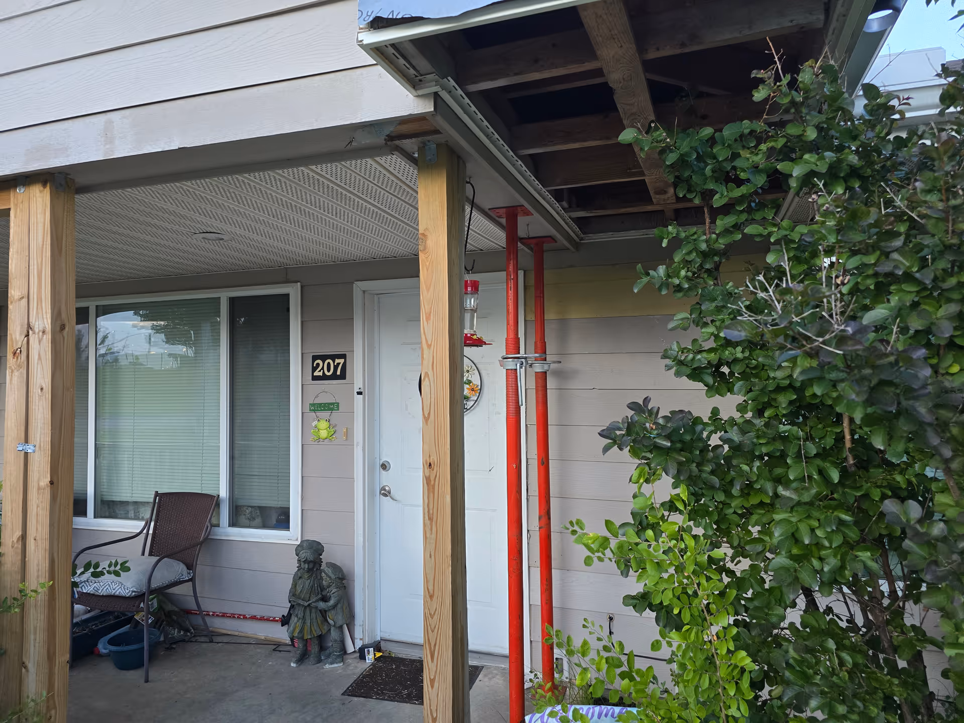 Exterior front entrance of a building with a porch, door 207, and greenery.