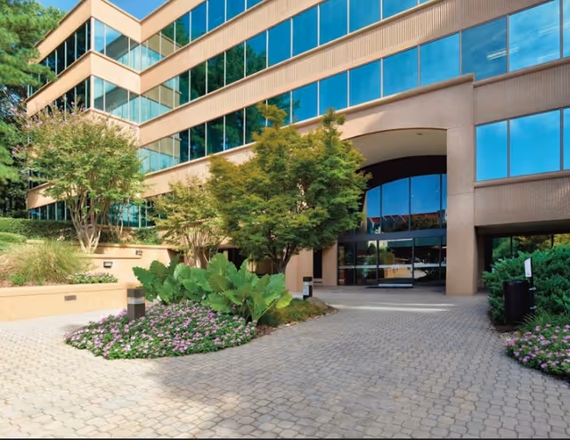 Exterior view of a modern building entrance with glass facade and landscaping.