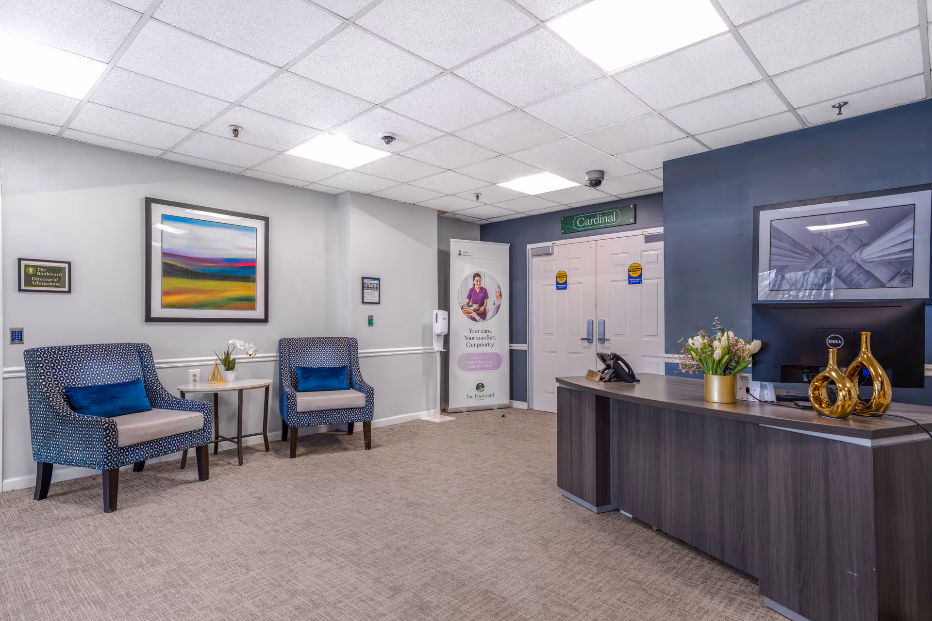 Interior lobby with two blue patterned chairs, a reception desk, and framed artwork.