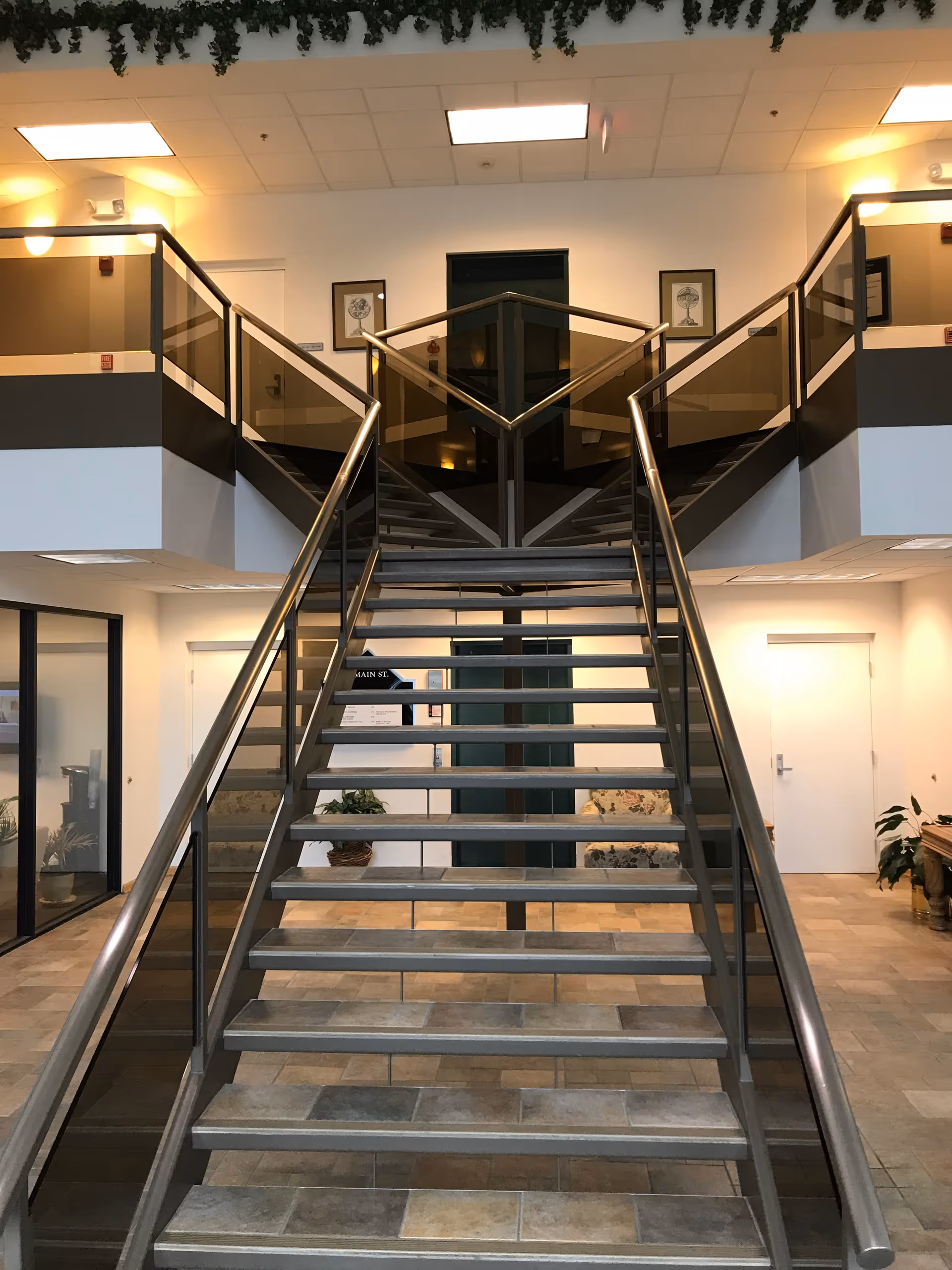 Interior stairwell in a senior living facility with a central metal staircase and glass railings.