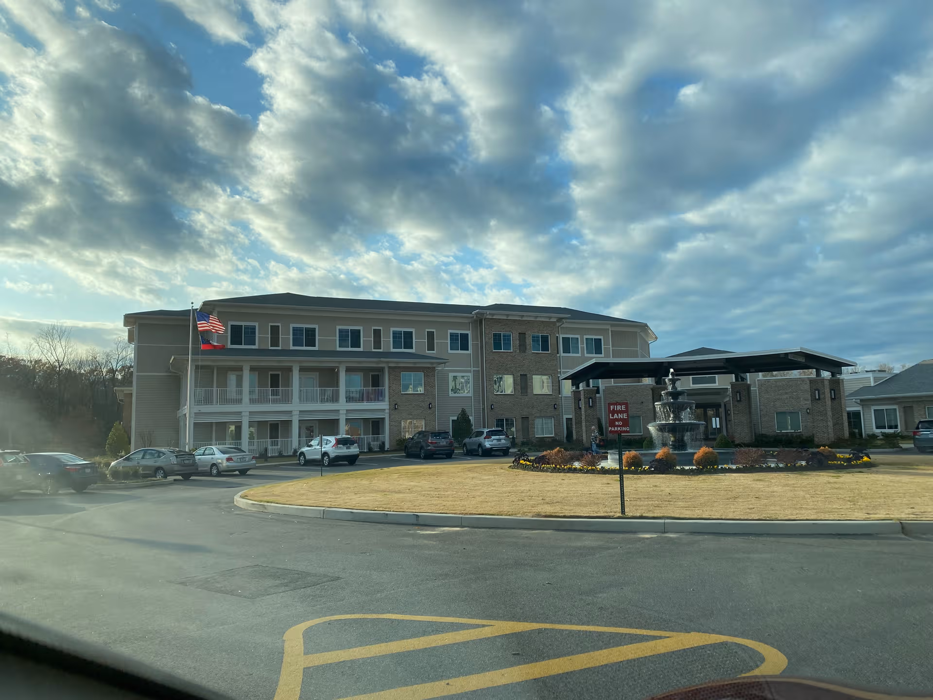 Exterior view of Watercrest Macon facility with a circular drive, fountain, and flag