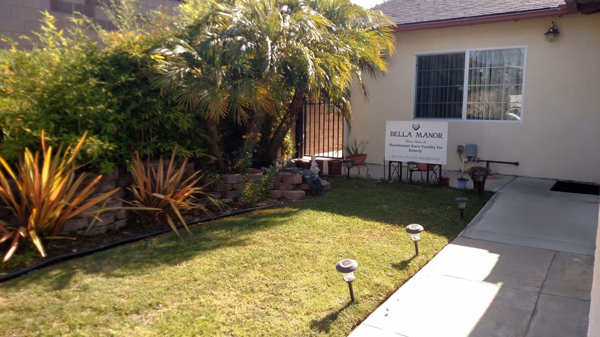 Front yard of Bella Manor with a sign, lawn, and landscaped plants.