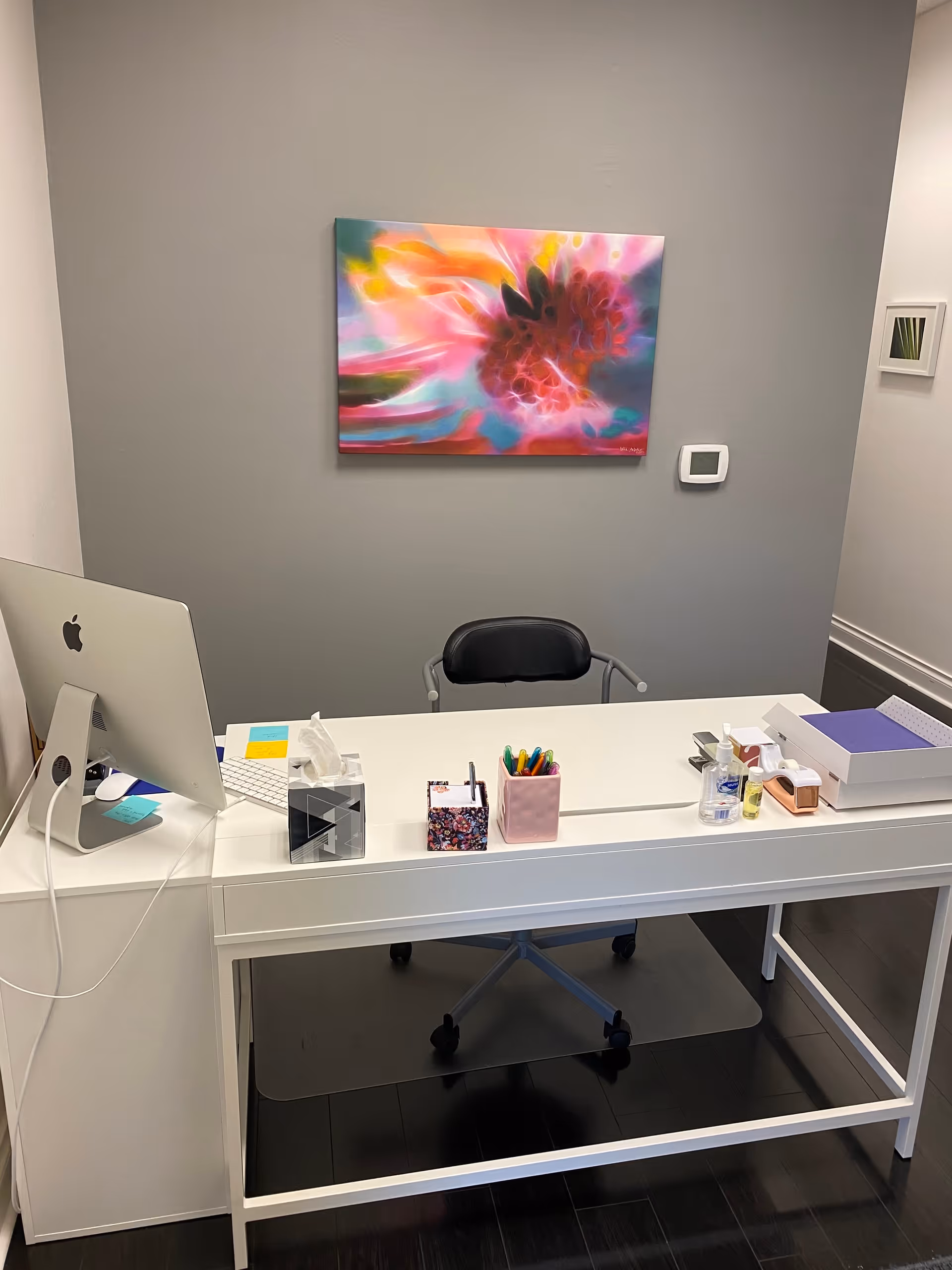 White desk with computer, organizers, and vibrant wall art in a clean office.