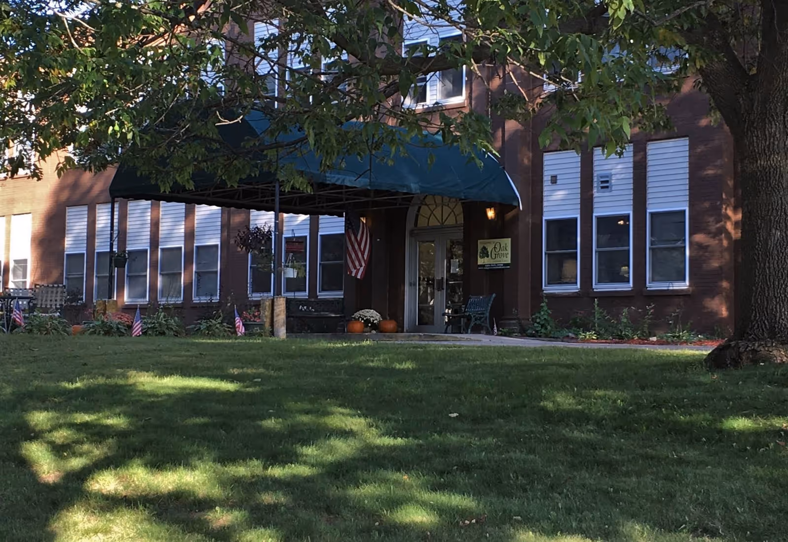Oak Grove Assisted Care entrance at a brick building with a green awning and lawn.