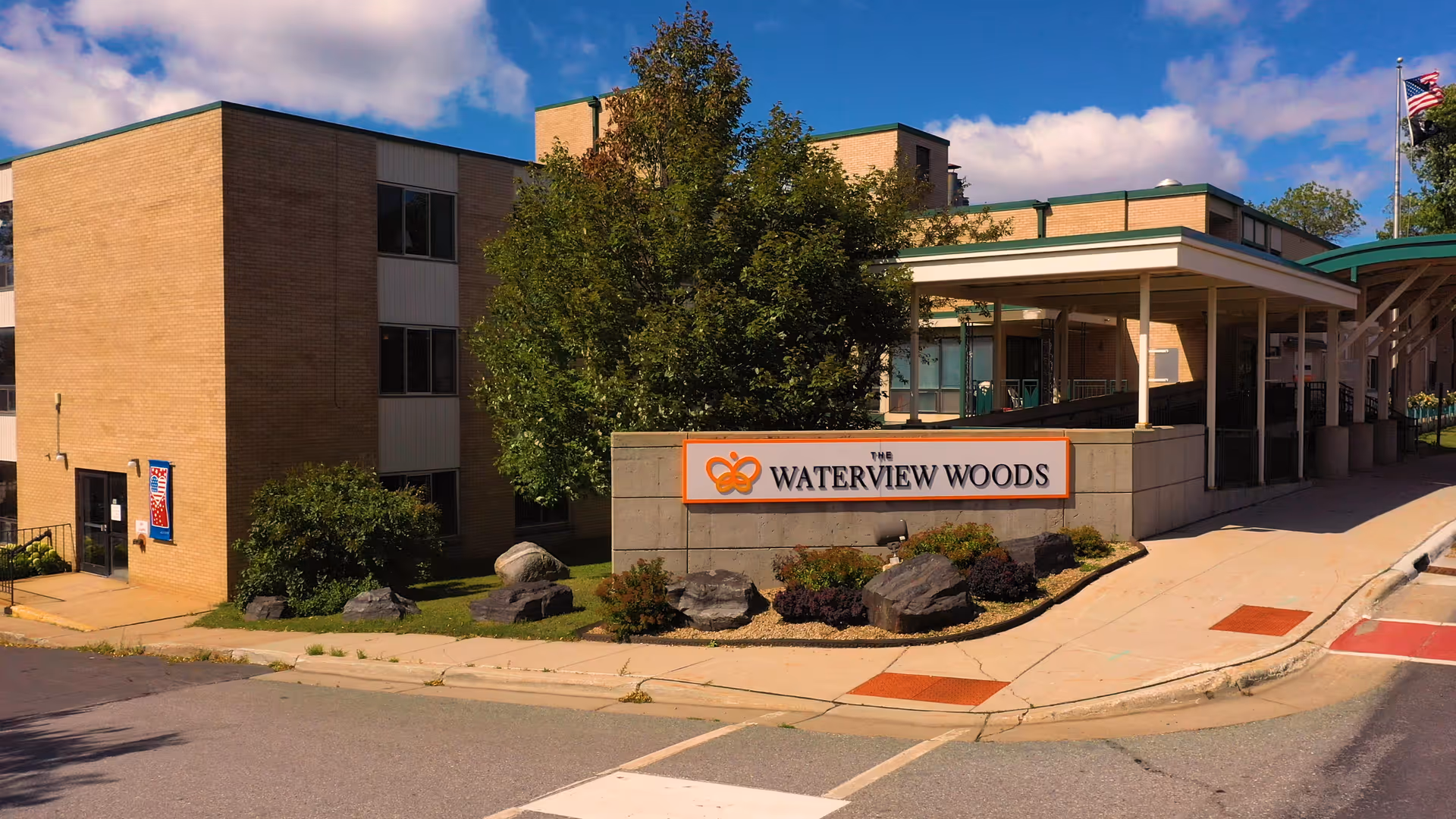 Front view of The Waterview Woods facility with sign, brick building, and landscaped entrance.