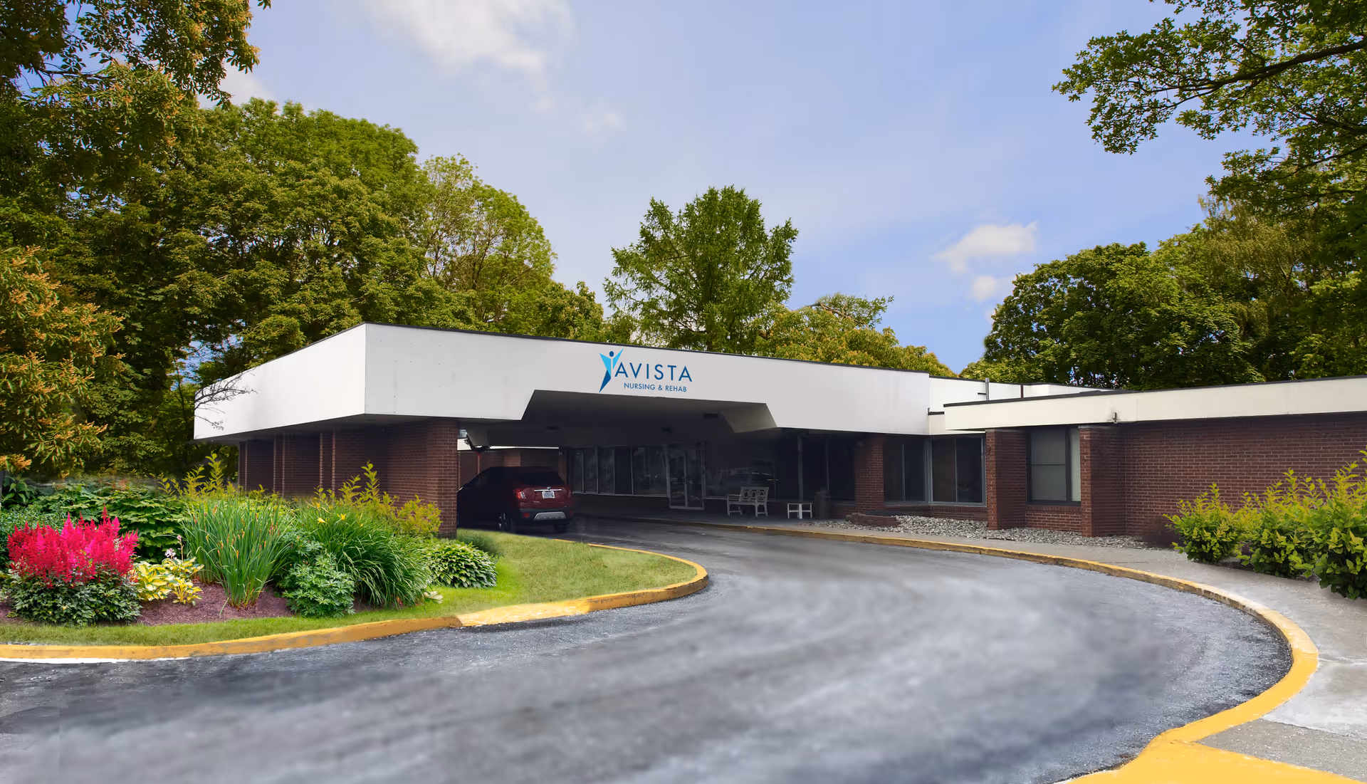 Covered entrance drive and drop-off at the Avista Nursing and Rehab building with landscaped beds and surrounding trees.