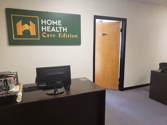 Reception desk with computer; green Home Health Care Edition sign on wall.