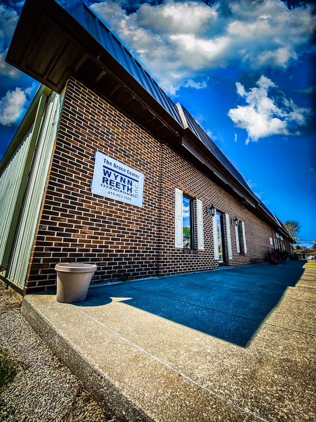 Brick exterior of Wynn-Reeth facility with walkway, sign, and clear blue sky.