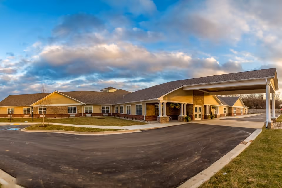 Exterior view of The Willows at Fritz Farm building with a covered entrance, parking area, and a partly cloudy sky.