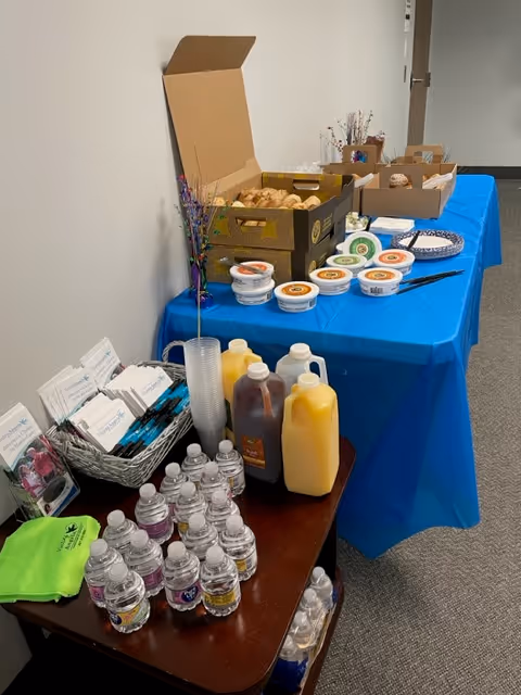 Refreshment table with a blue tablecloth, pastries, yogurt, and beverages in a hallway.