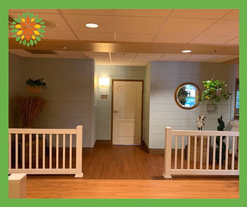 Interior common area with a centered white door, wood floors, white railing, potted plants and a round mirror on the wall.