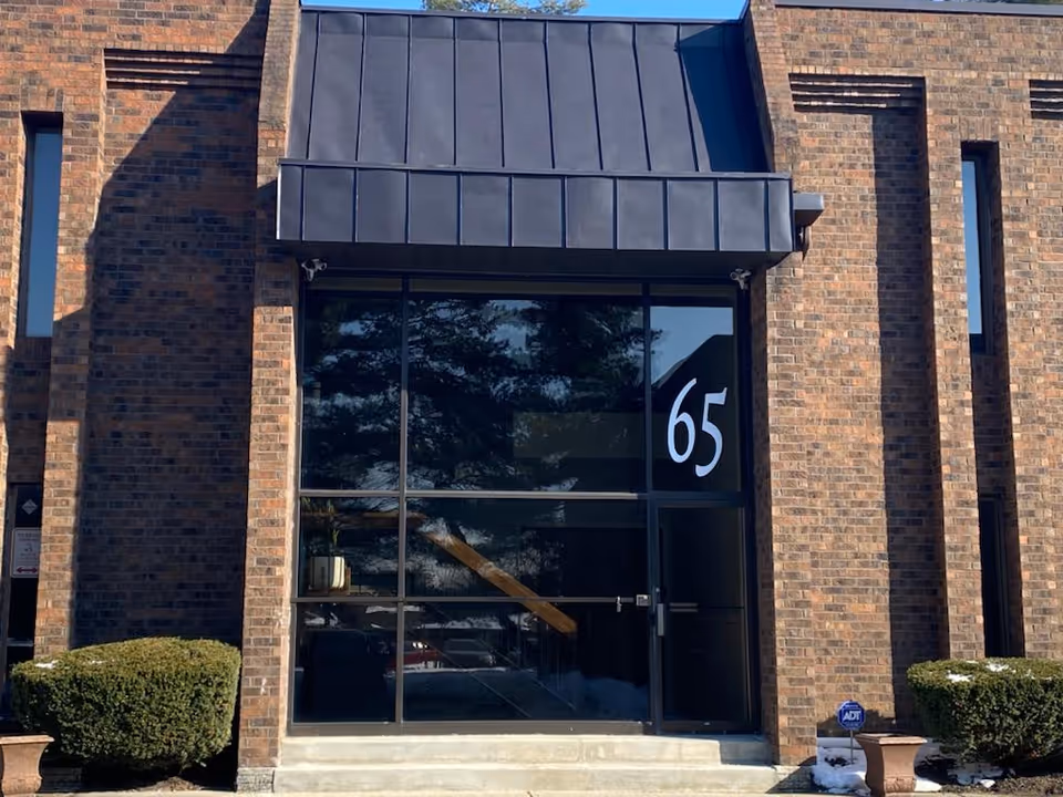 Front view of a brick building entrance with large glass doors and the number 65.