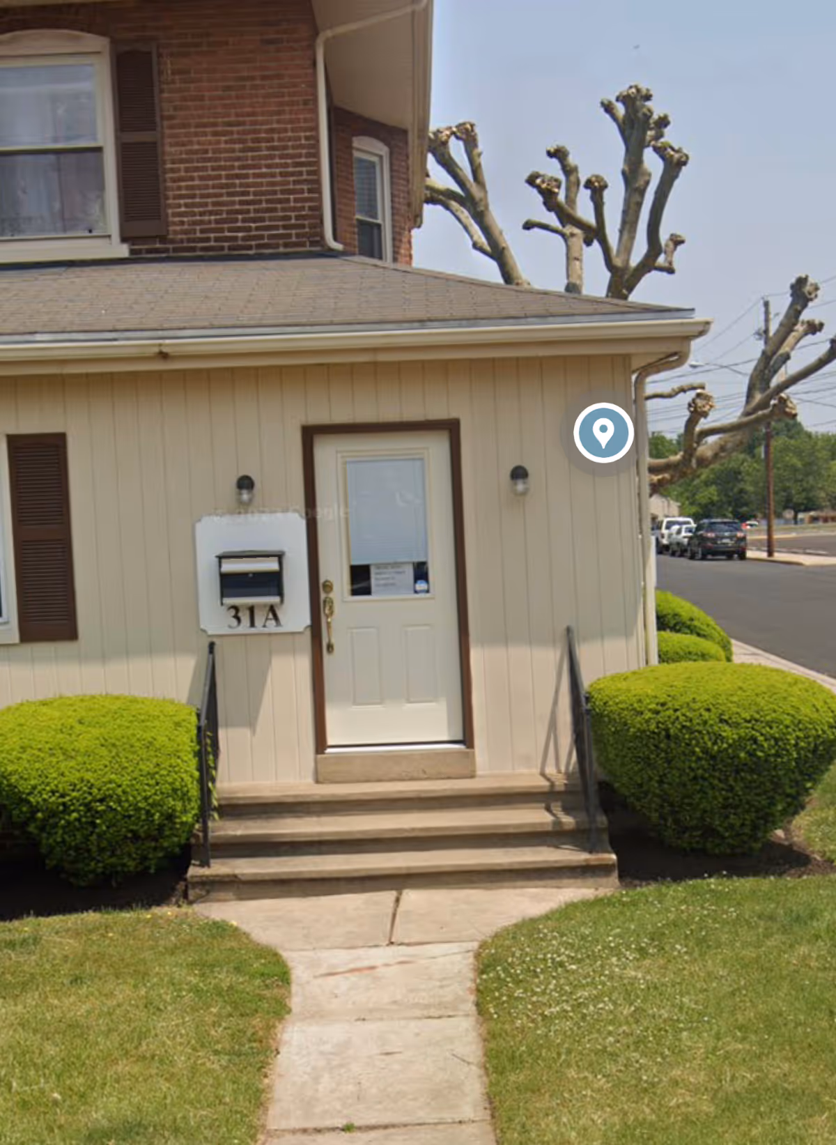 Entrance to a senior living facility with beige exterior, a front door, mailbox, and trimmed hedges.