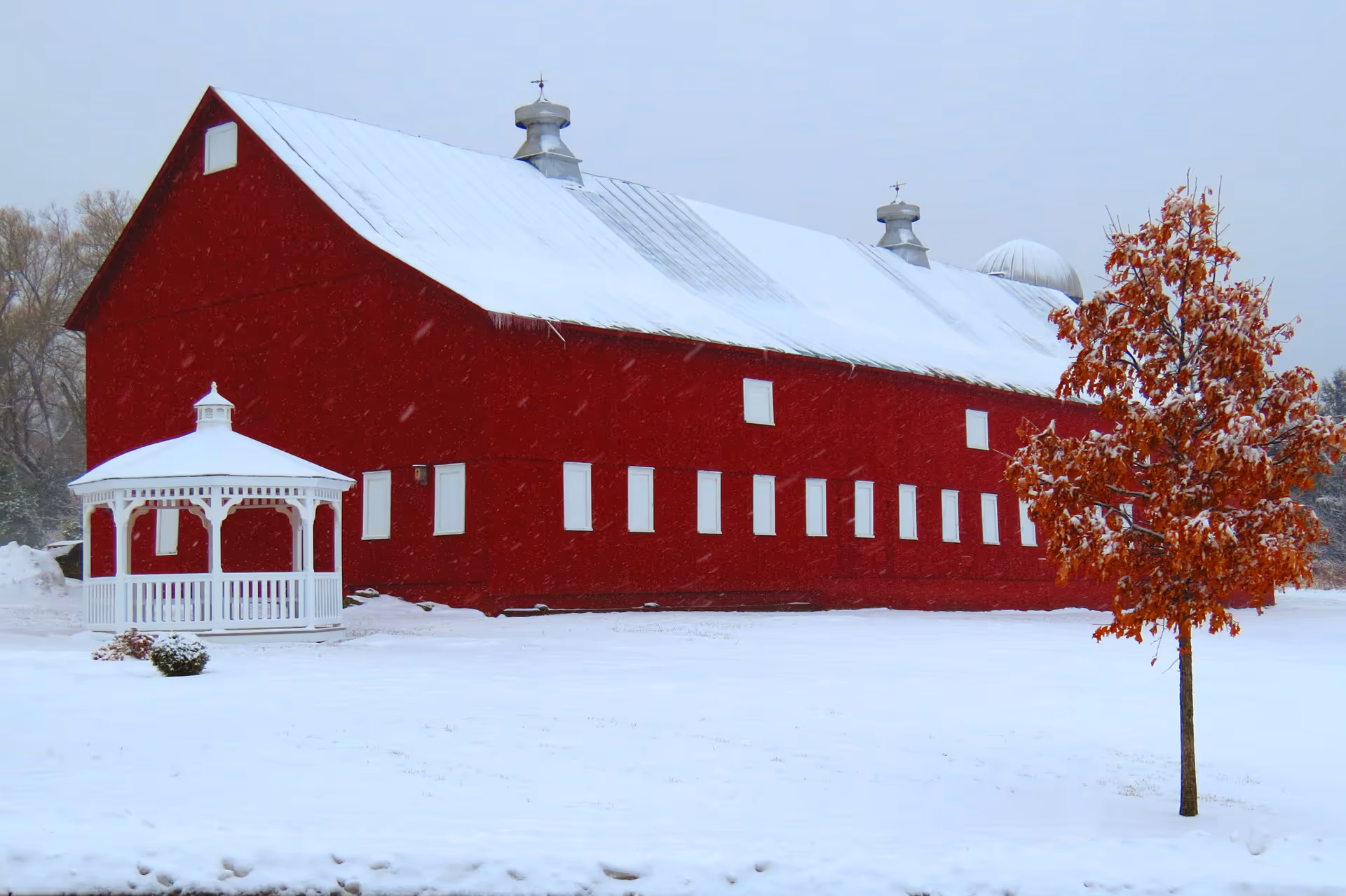 Snowy red barn-style building with a white gazebo in a rural setting.
