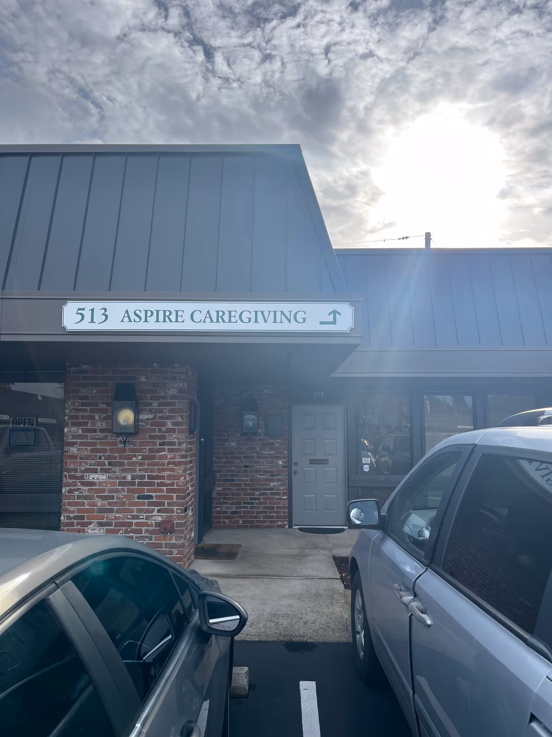 Front exterior of Aspire Caregiving with sign, brick facade, and parked cars.