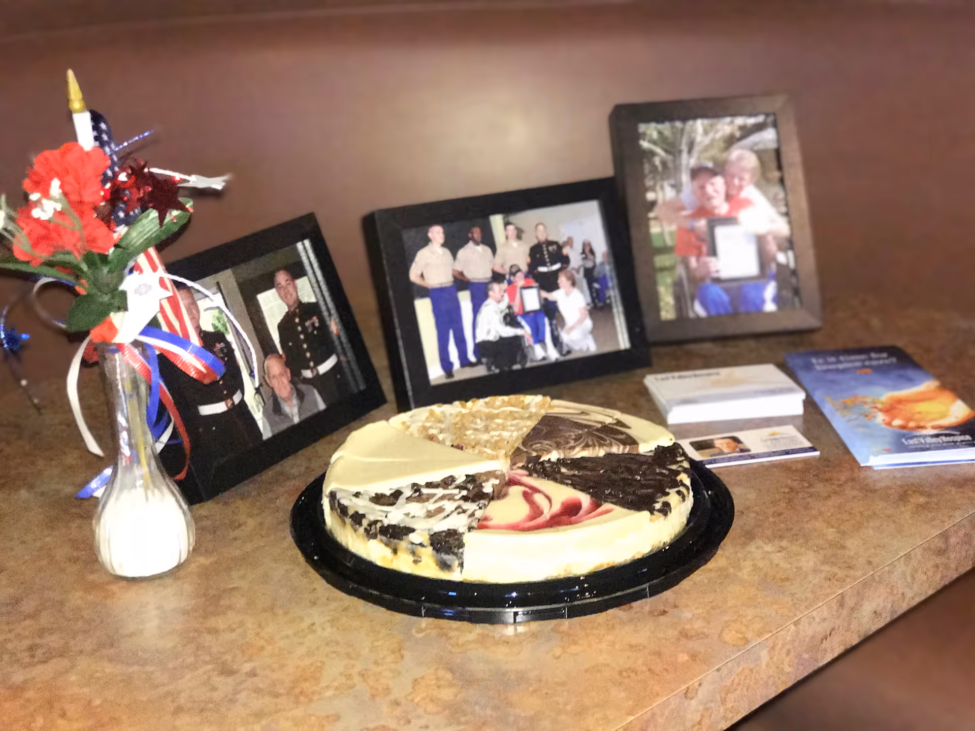Cake on a counter beside framed photos and brochures in a senior living lobby.