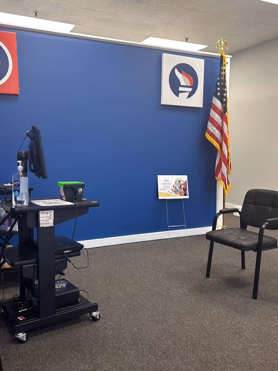 Interior reception area with blue wall, flag, desk, monitor, and a black waiting chair.