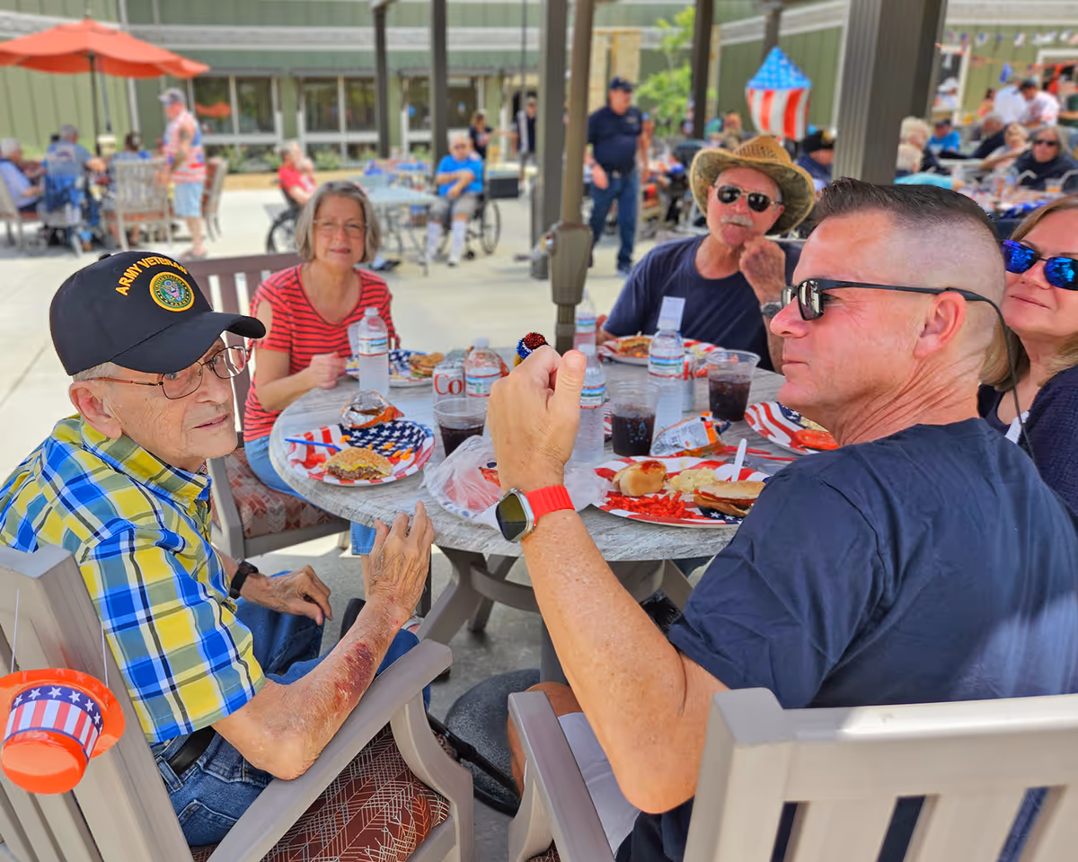 Group of elderly veterans dining outdoors at a round table with patriotic decorations.