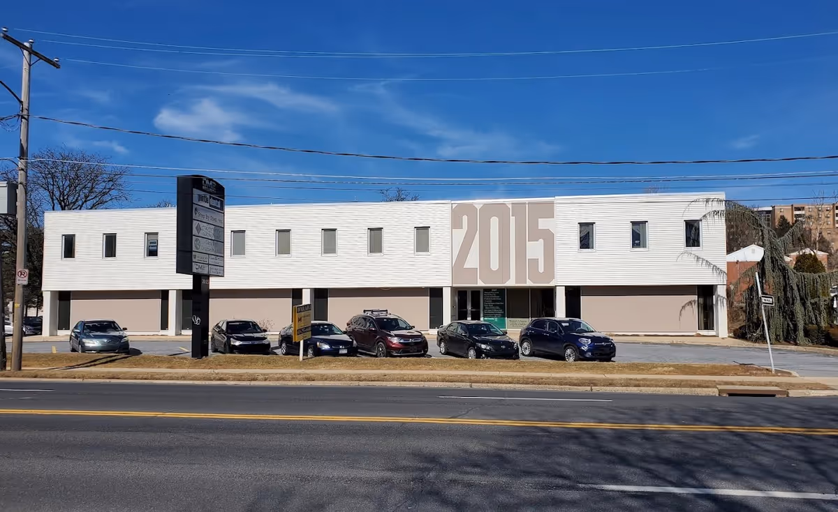 Modern two-story white building with a large 2015 sign and several cars parked outside.