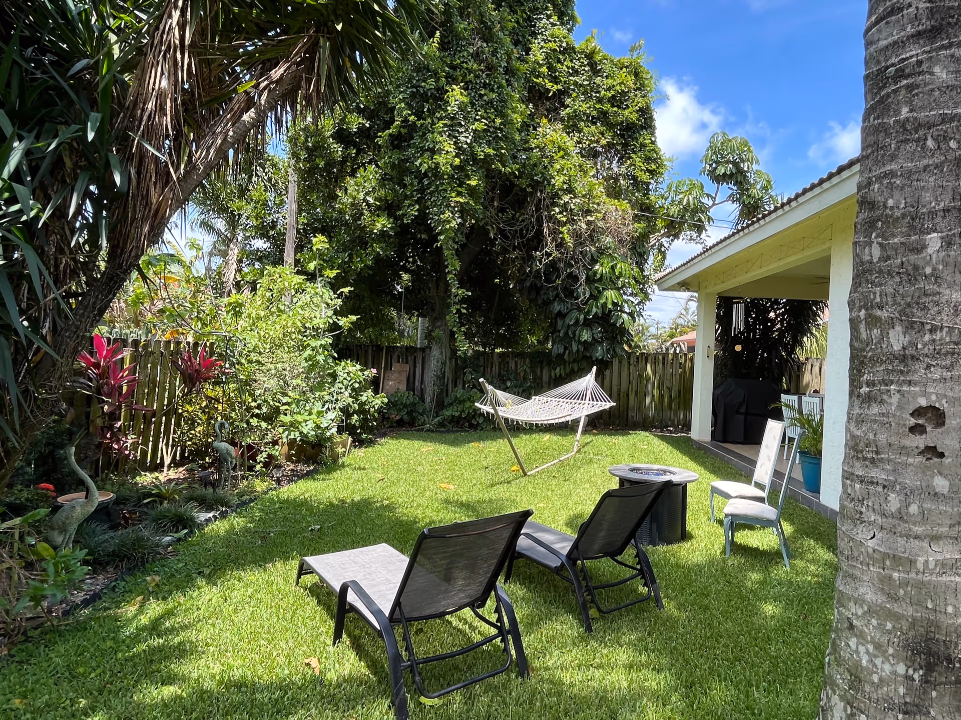 Sunlit backyard with lounge chairs, hammock, and a small covered patio area.