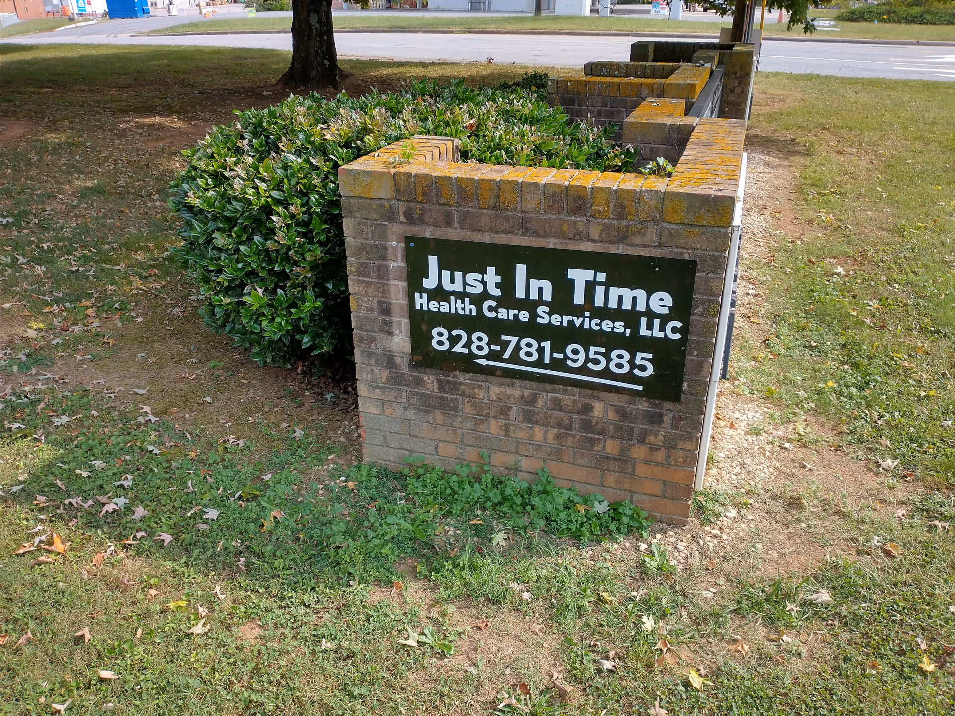Brick sign for Just In Time Health Care Services beside shrubbery and grassy lawn