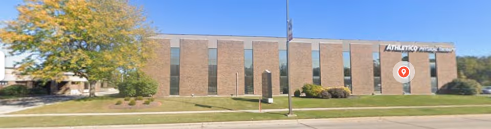 Brick senior living facility exterior with large windows, manicured landscaping, and a flagpole.
