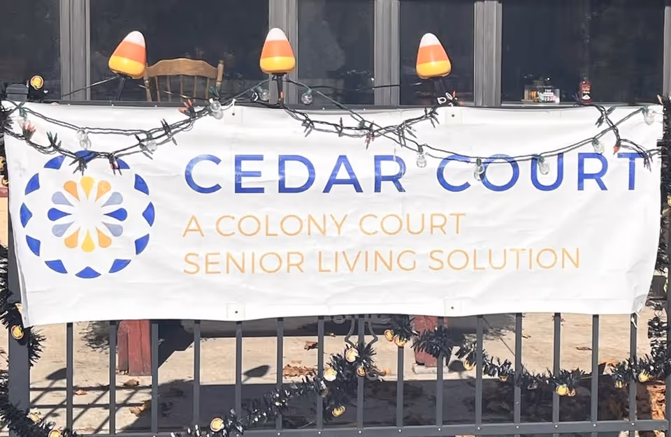 White banner reading Cedar Court, A Colony Court Senior Living Solution, hung on railing outside building.