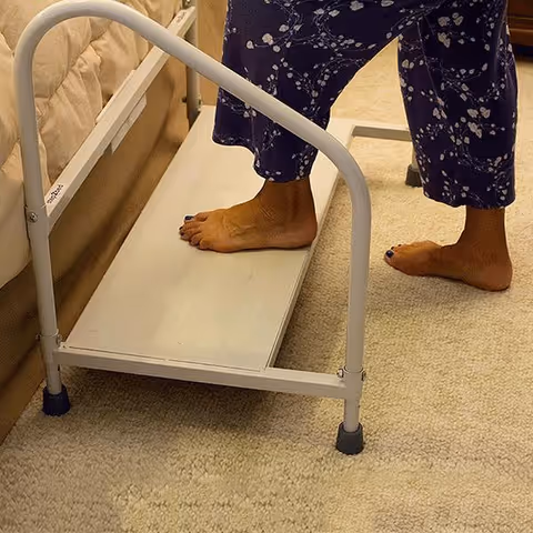 A person stands barefoot on a bed step stool beside a hospital-style bed.