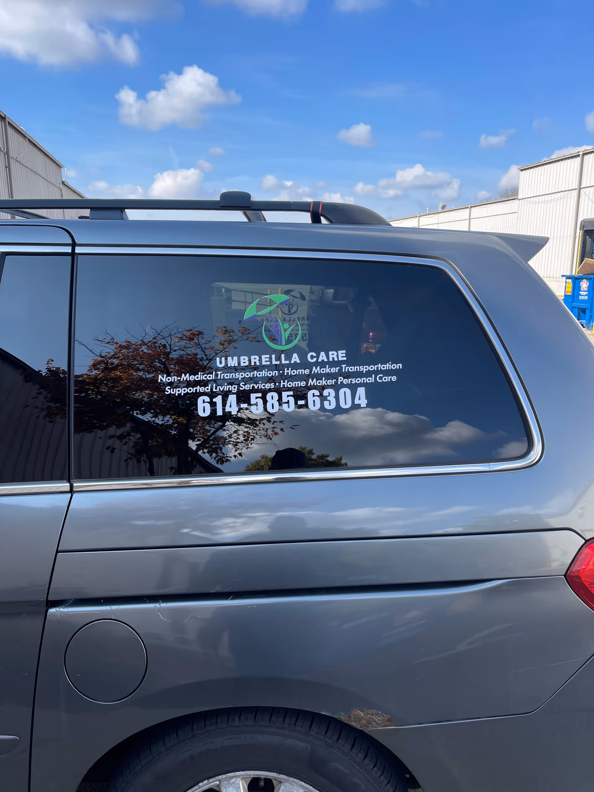 Rear side of a gray van displaying Umbrella Care Services logo and phone number.