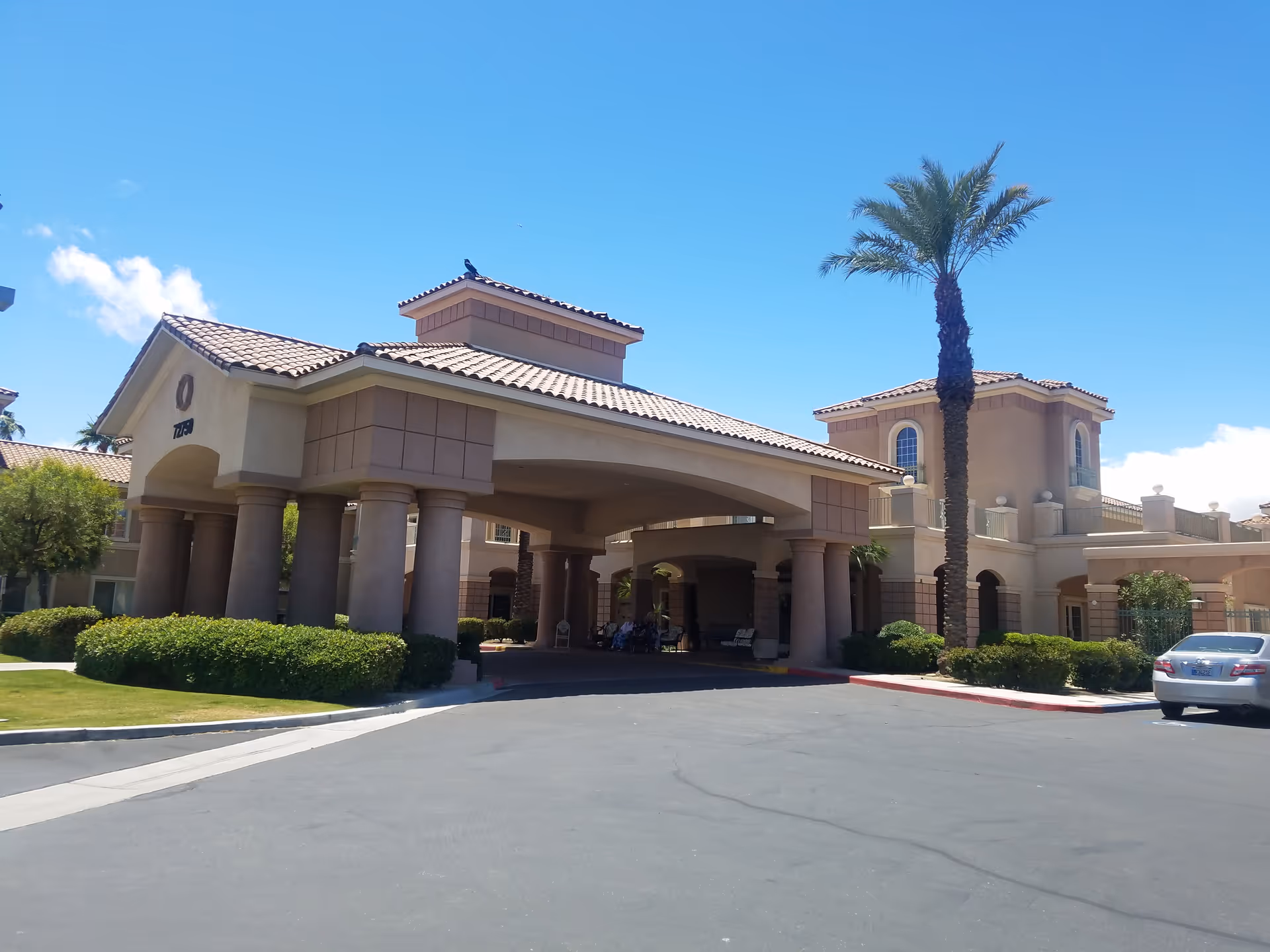 Senior living facility exterior with porte-cochere entrance and palm trees under a blue sky.