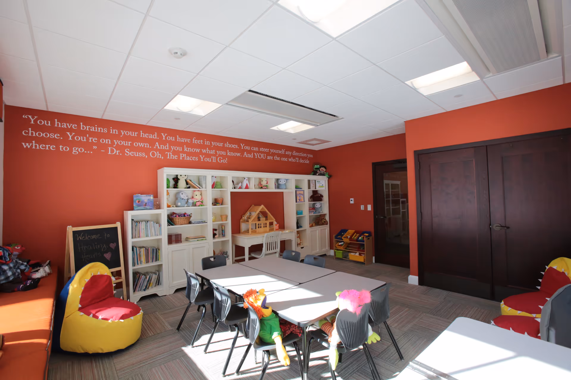 Bright playroom with shelves of toys, tables, and chairs in a red-walled interior.