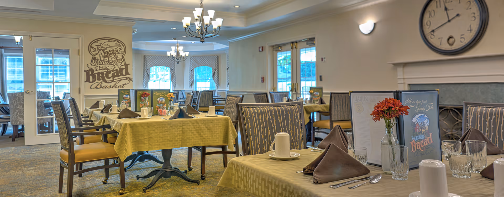Dining room in senior living facility with yellow tablecloths and a large wall clock
