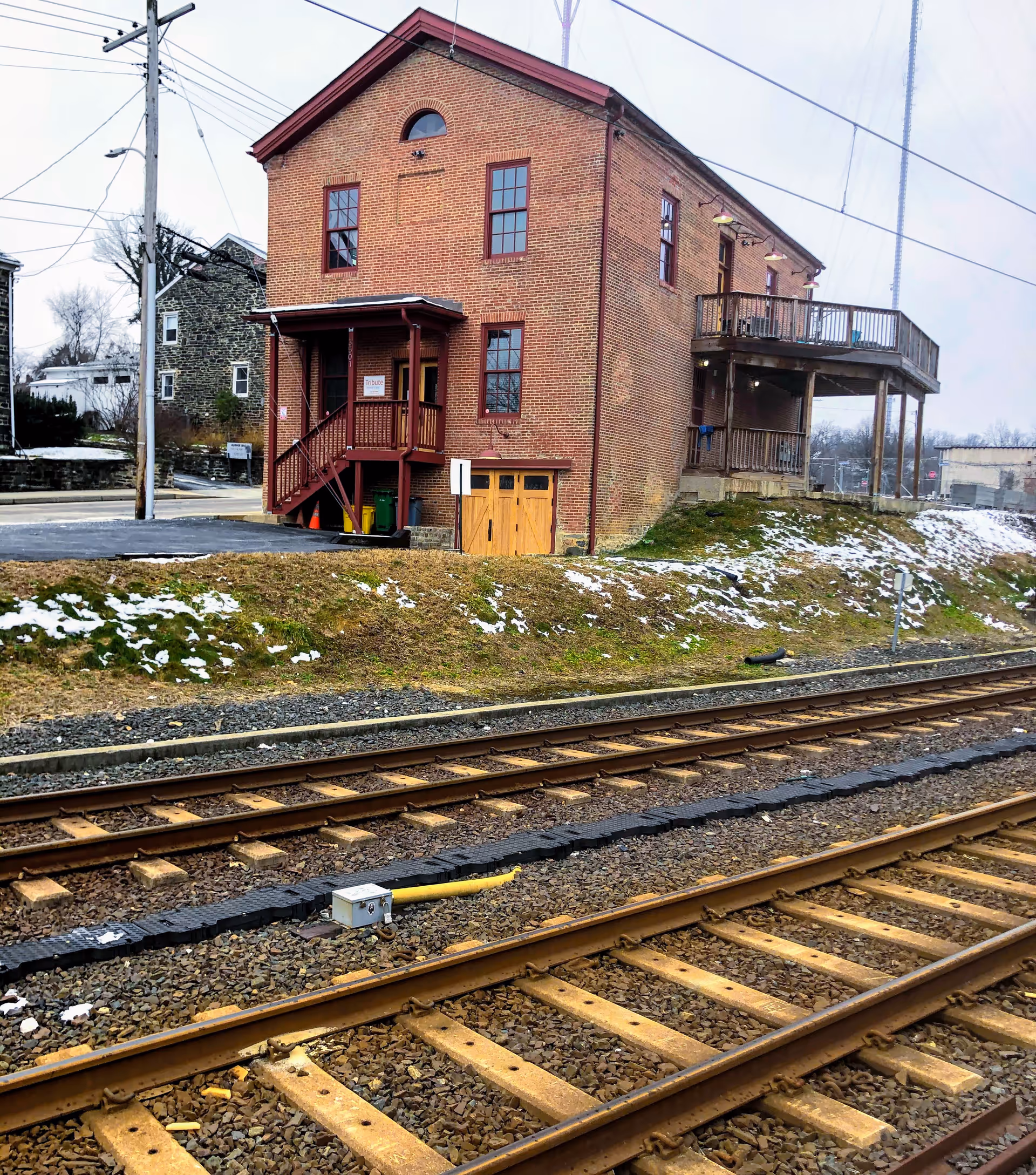 Brick two-story building near railroad tracks with stairs and a wooden balcony.