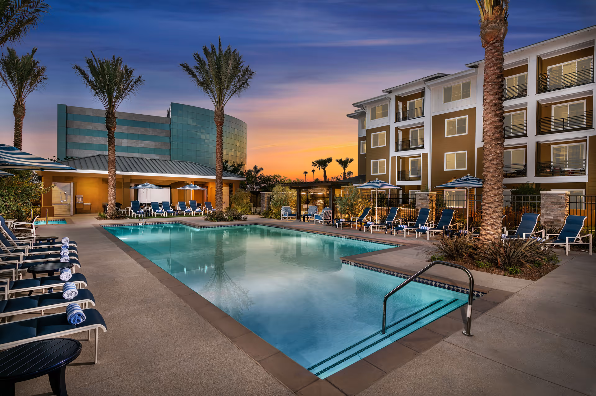 Outdoor pool area at Clearwater at Riverpark with lounge chairs, umbrellas, and palm trees.